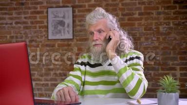 忙碌的、可爱的、长着胡子的白种人老人<strong>挂</strong>在<strong>电话</strong>上，一边看着电脑一边说着冷话